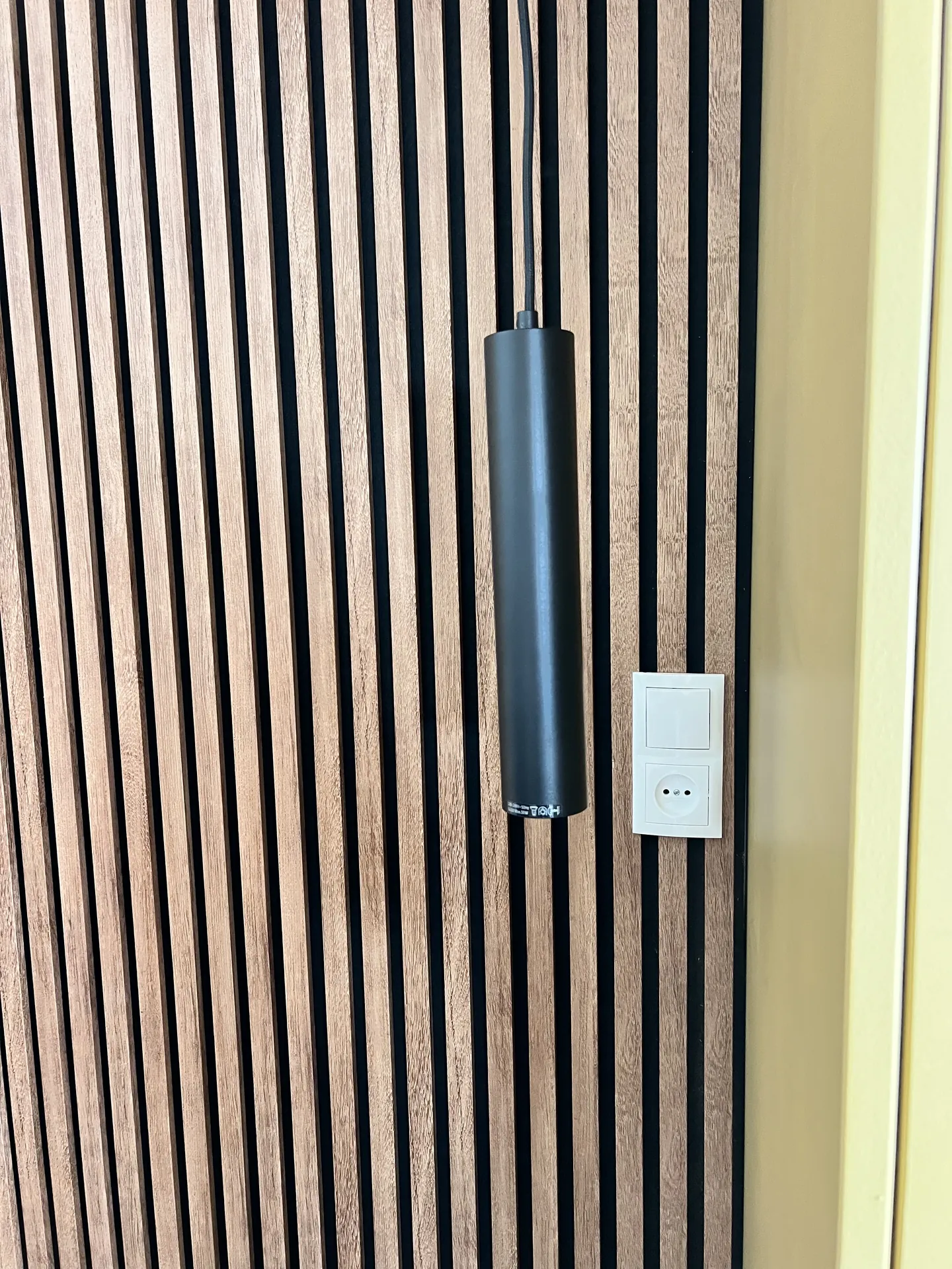 Lattenwand met hanglamp en stopcontact naast het bed