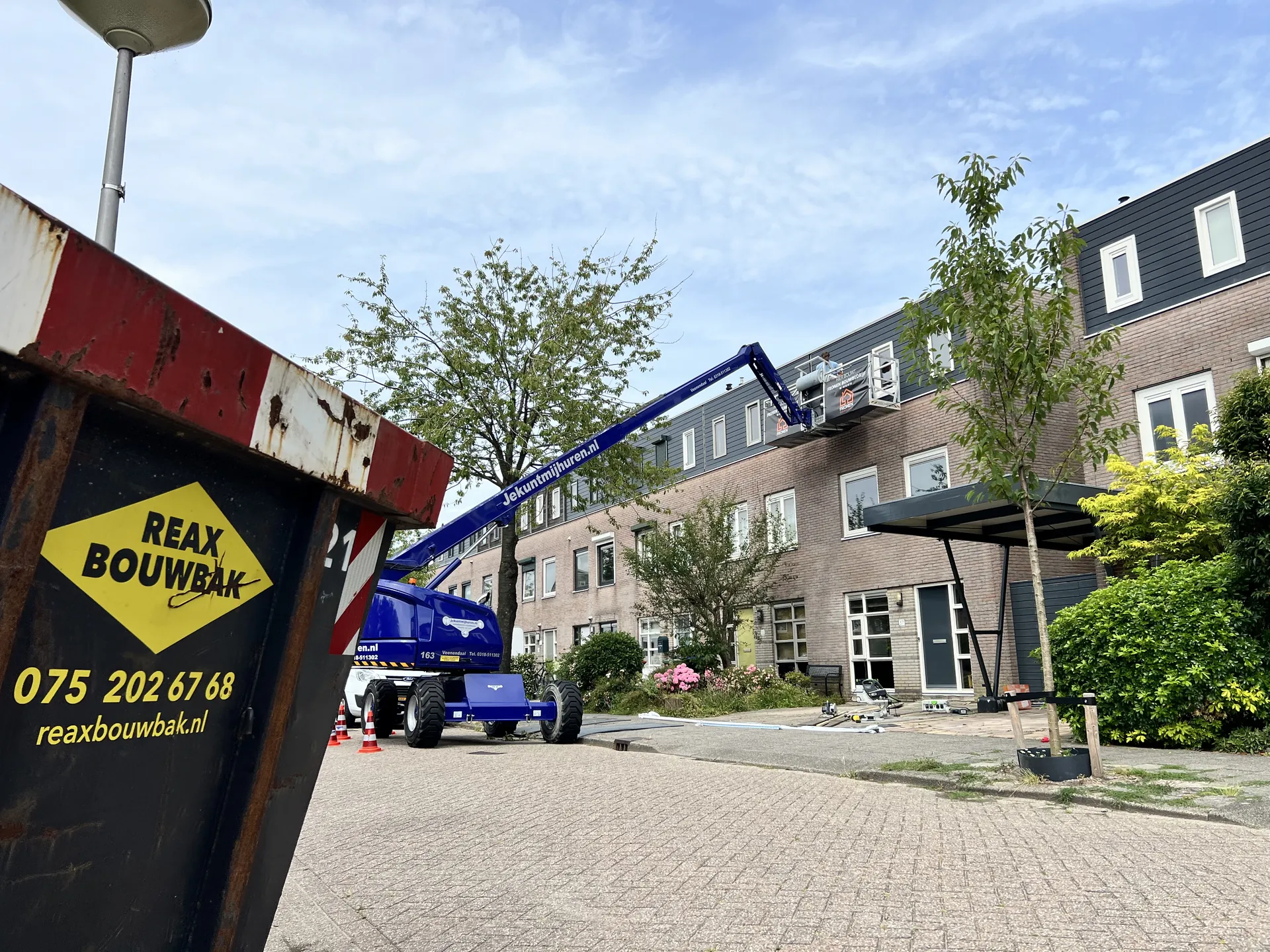 Hoogwerker en container bij de gevelrenovatie in Velserbroek